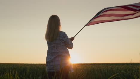 Glückliche-Frau,-Die-Amerikanische-Flagge-Auf-Weizenfeldhintergrund-Schwenkt.-4.-Juli---Unabhängigkeitstag-USA-Konzept