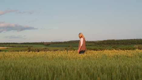 A-woman-walks-through-a-field-of-wheat-against-the-backdrop-of-a-picturesque-rural-landscape.-Side-view