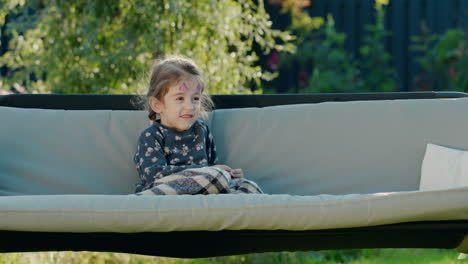 Portrait-of-a-cute-girl-with-face-painting-on-her-face,-resting-in-the-backyard-of-a-house-in-a-garden-swing