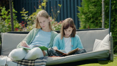 Zwei-Süße-Mädchen-Lesen-Bücher-Und-Sitzen-Auf-Einer-Gartenschaukel-Im-Hinterhof-Des-Hauses