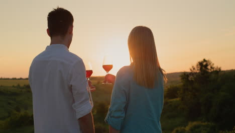 Junges-Paar-Mit-Einem-Glas-Rotwein,-Das-Den-Sonnenuntergang-über-Einem-Malerischen-Tal-Beobachtet