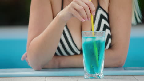 Beautiful-woman-in-a-swimsuit-stirs-ice-in-a-cocktail-on-the-edge-of-the-pool