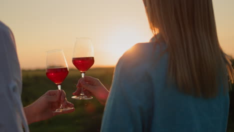 Young-couple-clinking-glasses-of-red-wine-against-the-backdrop-of-a-landscape-with-a-sunset
