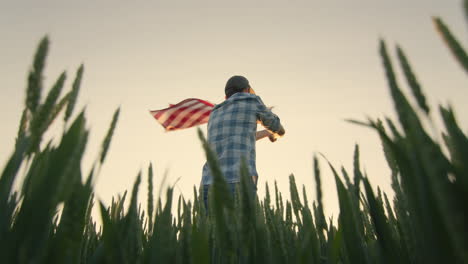 Silhouette-Eines-Jungen-Mannes,-Der-Die-Amerikanische-Flagge-Schwenkt.-Bei-Sonnenuntergang-Auf-Einem-Weizenfeld-Stehen.-Weitwinkelaufnahme-Aus-Niedrigem-Winkel