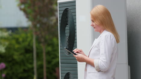 Woman-sets-up-a-heat-pump-near-a-private-house.-Uses-a-tablet