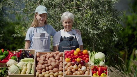 Portrait-of-an-elderly-farmer-woman-with-her-granddaughter.-Standing-behind-a-vegetable-stall-at-a-farmers'-market