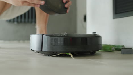 A-man-takes-out-a-trash-can-from-a-vacuum-cleaner-robot