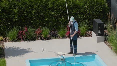 A-worker-cleans-a-swimming-pool-with-a-special-vacuum-cleaner.-Top-view