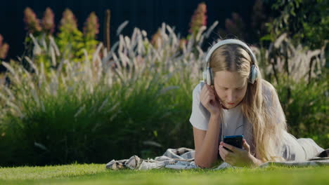 A-teenager-with-a-smartphone-and-headphones-lies-on-the-grass-in-the-park
