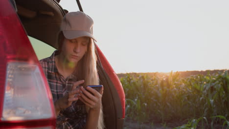 Süßes-Teenager-Mädchen-Sitzt-Im-Kofferraum-Eines-Autos-Und-Benutzt-Ein-Smartphone.