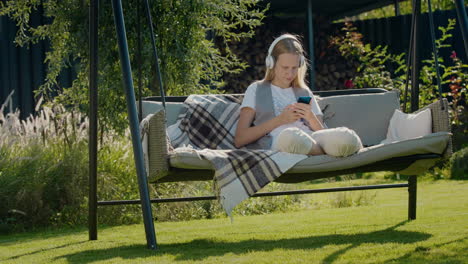 A-teenage-girl-is-resting-on-a-garden-swing,-using-a-smartphone.