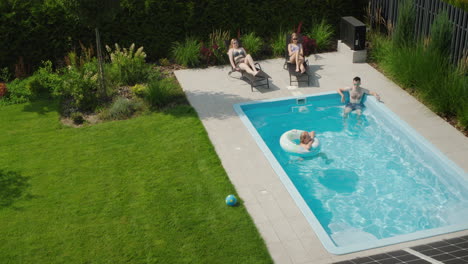 A-family-relaxes-in-the-pool,-in-the-foreground-are-panels-of-a-solar-power-plant-on-the-roof-of-a-cottage