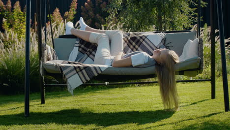 A-girl-with-long-hair-lies-on-a-garden-swing,-relaxes-on-a-hot-summer-day