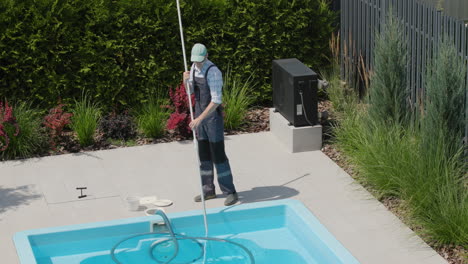 A-worker-in-uniform-cleans-the-pool-with-a-vacuum-cleaner,-removes-dirt-from-the-bottom.-Tilt-shot