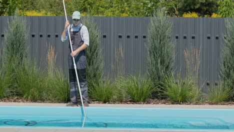 Worker-in-overalls-vacuuming-the-pool-in-the-backyard-of-the-house