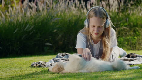 Teenage-girl-plays-with-a-puppy,-lies-on-the-lawn,-listens-to-music-on-headphones