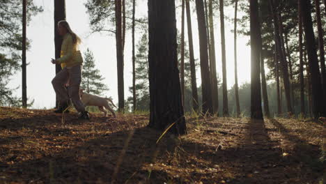 Girl-running-through-the-forest-with-a-golden-retriever-puppy,-having-a-good-time-and-having-fun