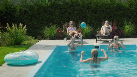 A-friendly-family-is-relaxing-by-the-pool,-playing-ball.-Having-a-good-time-together-on-a-hot-summer-day