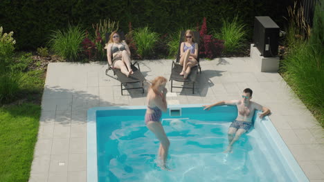 A-cheerful-family-is-relaxing-by-the-pool,-a-woman-jumps-into-the-water.-Enjoying-a-warm-summer-day