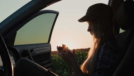 Silhouette-of-a-teenager-with-a-phone.-Sitting-in-the-passenger-seat-in-front-of-a-field-of-corn.