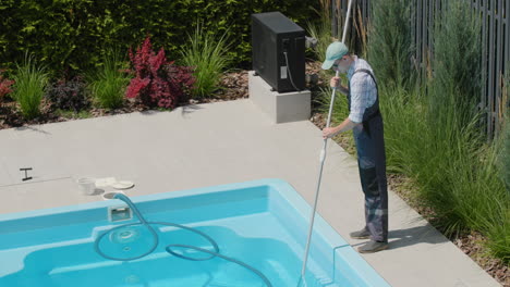 A-worker-in-uniform-cleans-the-pool-with-a-vacuum-cleaner,-removes-dirt-from-the-bottom