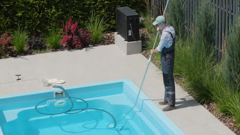 Worker-in-overalls-vacuuming-the-pool-in-the-backyard-of-the-house.-Top-view