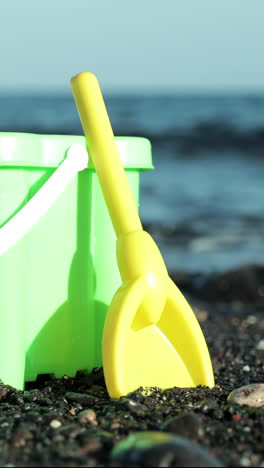plastic-bucket-and-spade-on-a-black-sand-beach-with-the-ocean-in-vertical