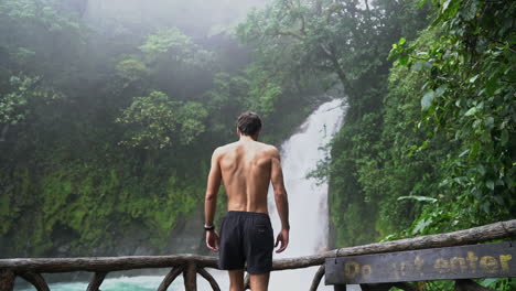 Mann-Geht-Zur-Schiene-Mit-Blick-Auf-Den-Rio-Celeste-Wasserfall-Costa-Rica,-Zeitlupe