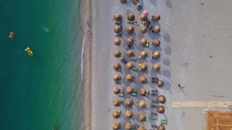 Clean-beach-with-straw-umbrellas-near-turquoise-sea-water,-top-down-shot-at-golden-hour