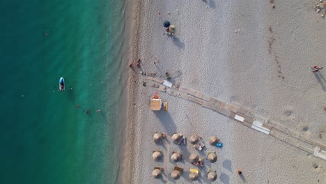 Summer-vacation-on-beautiful-beaches-in-Albania,-tourists-sunbathe-under-umbrellas-near-turquoise-seawater