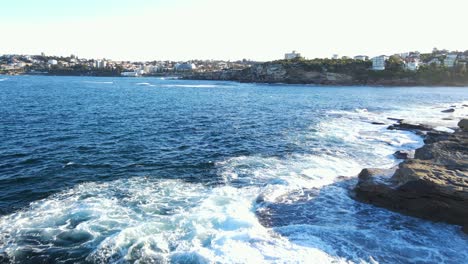 Ocean-Waves-At-The-Rocky-Seashore-Of-Clovelly-Bay-With-A-View-Of-The-Eastern-Suburbs-In-Sydney,-Australia
