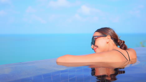 Woman-in-Sunglasses-Relaxing-Leaning-her-Head-on-the-Hands-in-the-Border-of-Infinity-Pool,-daytime-Miami