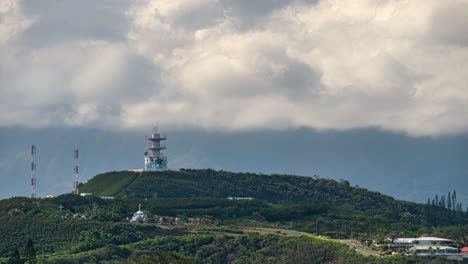 Time-lapse-shot-of-clouds-rolling-over-a-radio-tower-on-a-green-hill,-in-Noumea