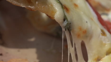 Picking-up-a-slice-of-fresh-delicious-pizza-with-the-cheese-stretching-as-it-pulls-apart---close-up