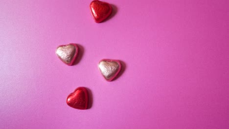 Decorative-shiny-foil-wrapped-love-heart-shaped-sweet-candy-stop-motion-pink-colourful-background
