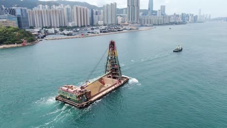 Tugboat-pulling-a-barge-loaded-with-fresh-excavated-Sand-along-Hong-Kong-coastline,-Aerial-view