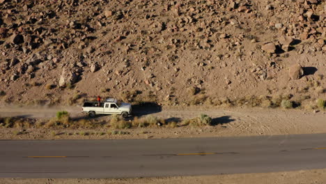 Pickup-driving-un-gravel-road-in-desert-landscape-with-person-standing-on-the-back-bed
