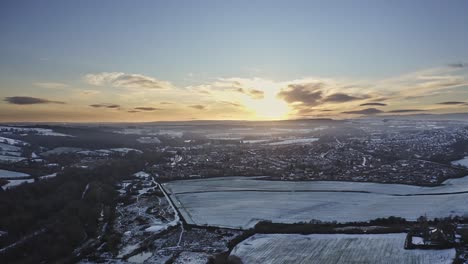 Drone-flight-over-a-small-Yorkshire-town-covered-in-snow-at-sunset,-aerial-view