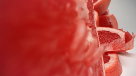 Grapefruit-slice-spins-and-falls-over-into-pile-of-grapefruit-closeup-pull-away-through-the-center-of-grapefruit-section-product-food-video-4k