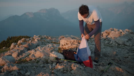 Auf-Dem-Berg-Peca-Holt-Ein-Junger-Wanderer-Am-Frühen-Morgen-Eine-Slowenische-Flagge-Aus-Seinem-Rucksack
