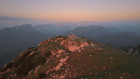 Drohnenaufnahme-Von-Der-Spitze-Des-Berges-Peca-Am-Sunrse,-Wo-Ein-Wanderer-Eine-Slowenische-Flagge-An-Der-Stange-Hält