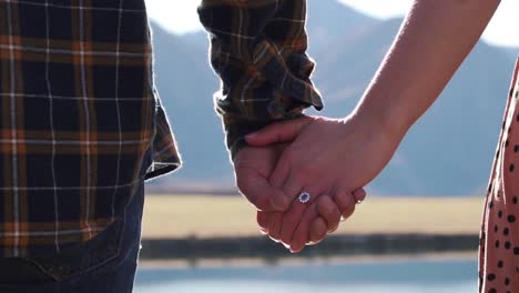 Couple-in-love-holding-hands-after-getting-engaged-with-engagement-ring-on-finger-looking-out-onto-beautiful-lake-view