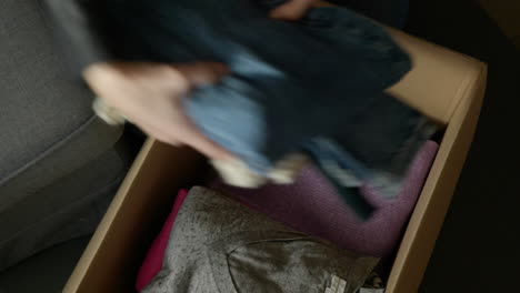 Woman-packing-folded-clothes-into-cardboard-box-preparing-for-new-home-move