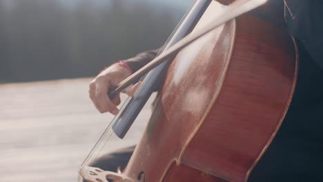 Close-up-of-a-cello-player,-playing-pizzicato-style-outdoors-in-a-warm-autumn-scenery-wearing-a-black-shirt