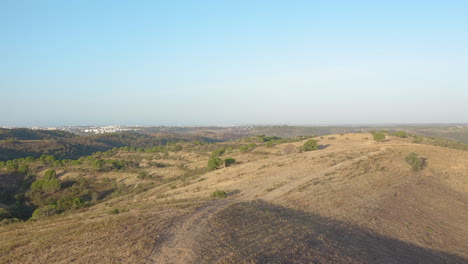 Aerial-tracking-shot-backwards-of-dirt-trail-on-top-of-a-barren-hill-in-Algarve,-Portugal