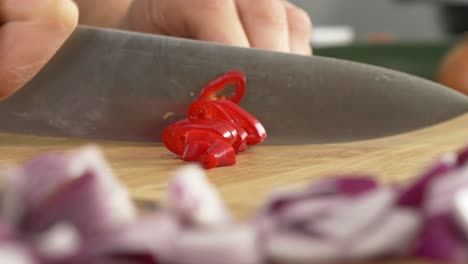 Slicing-red-pepper-on-a-wooden-table-top-with-a-big-chef's-knife