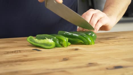 Slicing-green-peppers-on-a-wooden-table-top-with-a-chef's-knife