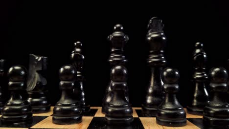 Truck-shot-from-right-to-left-of-black-chess-pieces-standing-on-a-chessboard-on-a-black-background