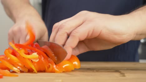 Slicing-red-peppers-on-a-wooden-table-top-with-a-chef's-knife