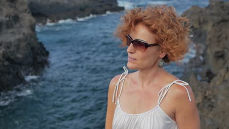 A-slow-motion-close-up-shot-of-a-redhead-elegant-woman-with-sunglasses-in-a-cliff